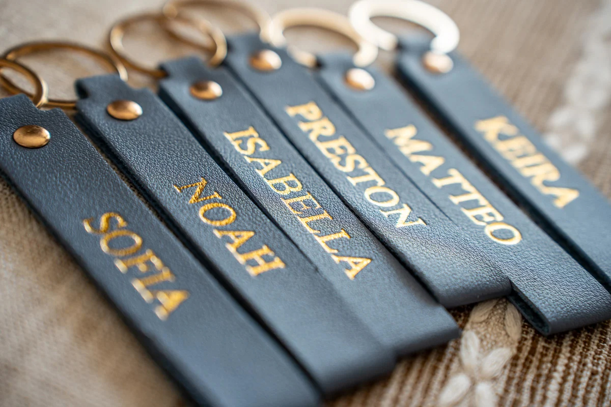 Six navy leather keychains, each foil stamped with a different first name in gold
