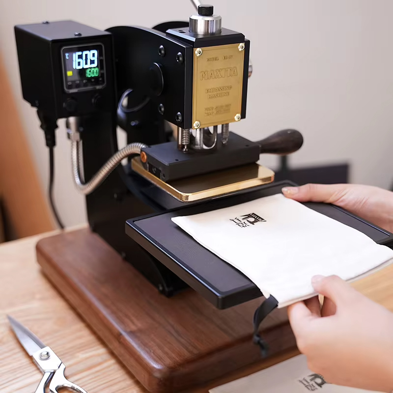 A technician feeding a leather piece into a hand operated hot foil press heated to 160 degrees