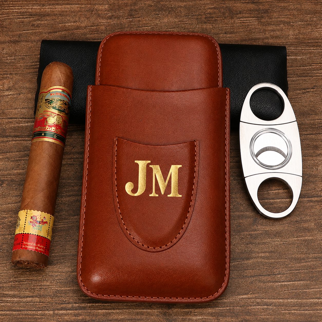 Brown leather cigar holder hot foil stamped with gold JM initials beside a cigar and cutter