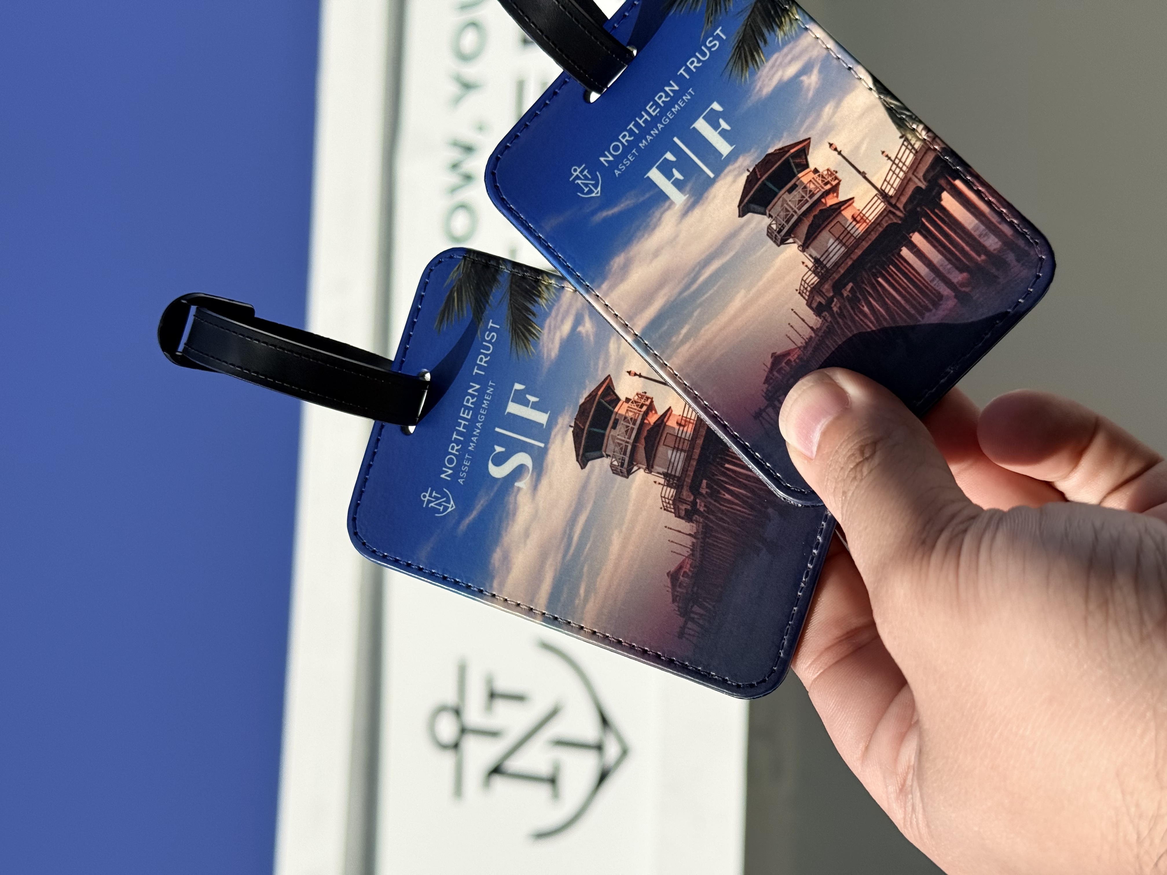 Two special edition Northern Trust luggage tags monogrammed S F and F F held in front of the booth signage